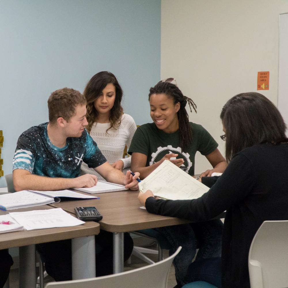 Five people sit at a table and work on homework 